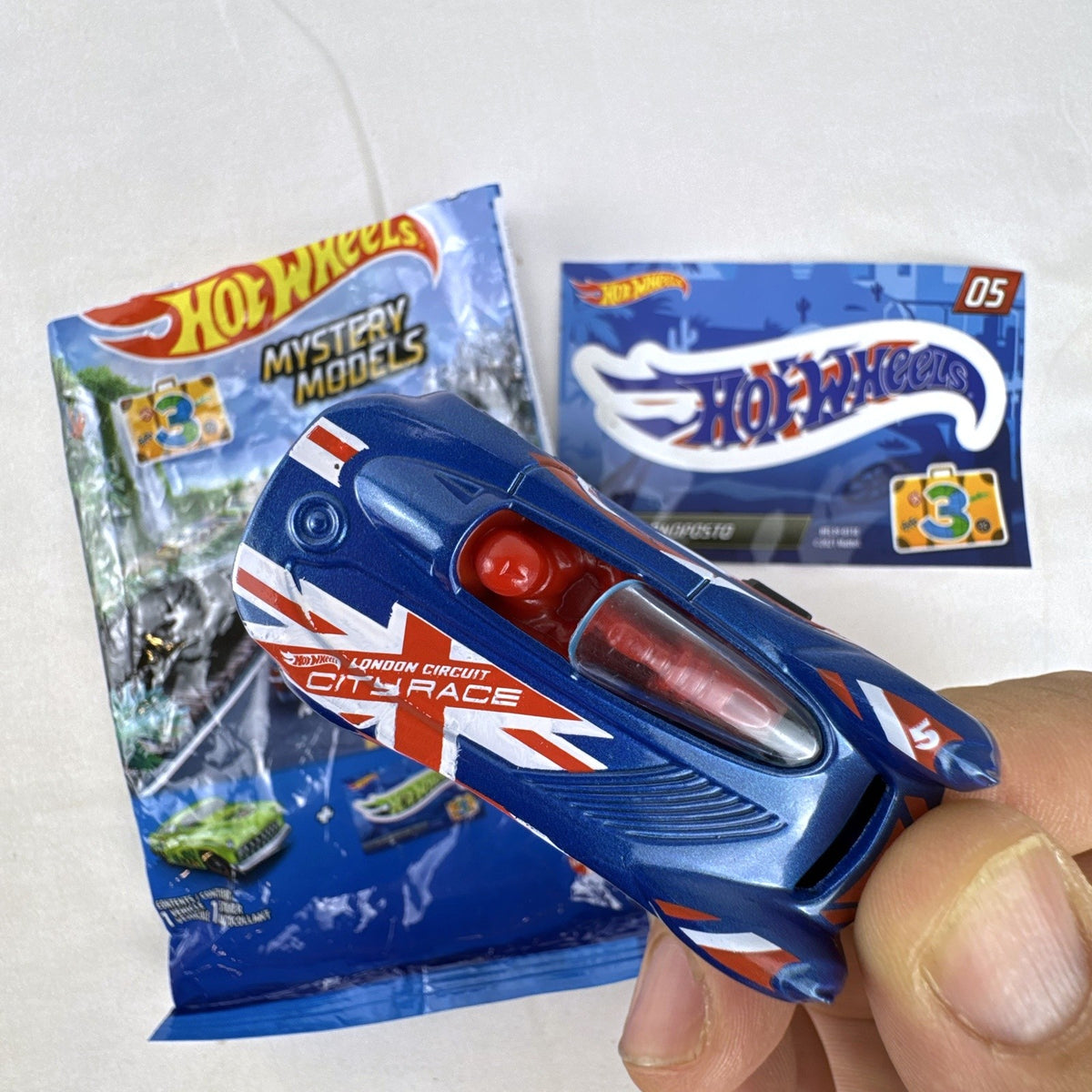 Hot Wheels Monoposto Mystery Models Series 3 #05 blue diecast car with Union Jack livery, original bag, and sticker card.