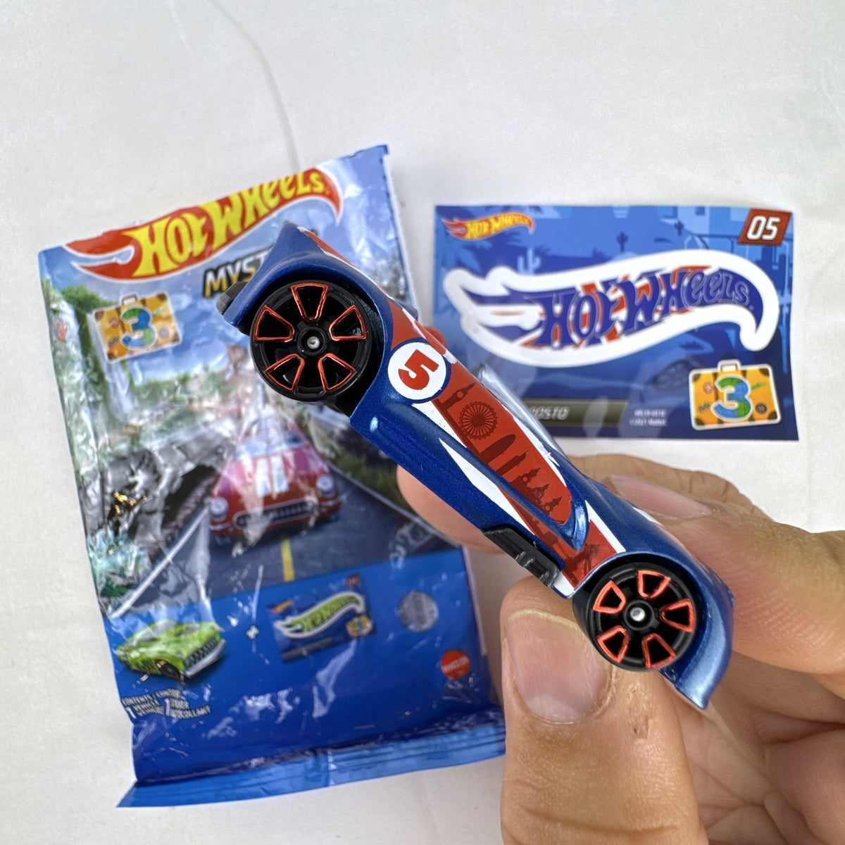 Hot Wheels Monoposto Mystery Models Series 3 #05 blue diecast car with Union Jack livery, original bag, and sticker card.