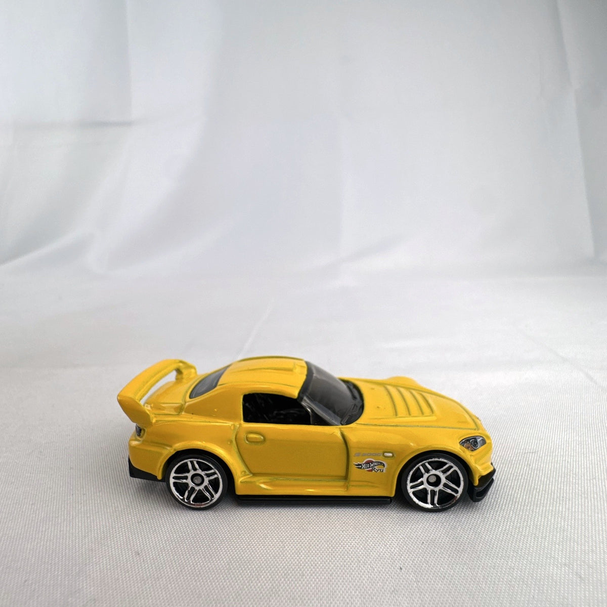 Yellow 1:64 scale Hot Wheels Honda S2000 diecast car featuring Ryu Asada tribute graphics