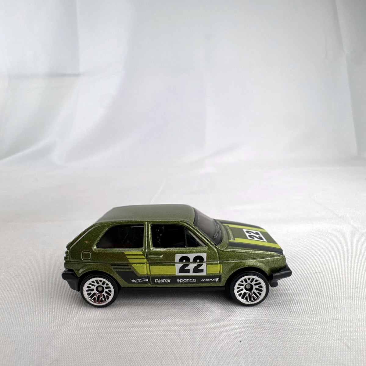 Hot Wheels 1:64 scale Volkswagen Golf Mk2 diecast car in metallic olive green with Castrol racing livery.