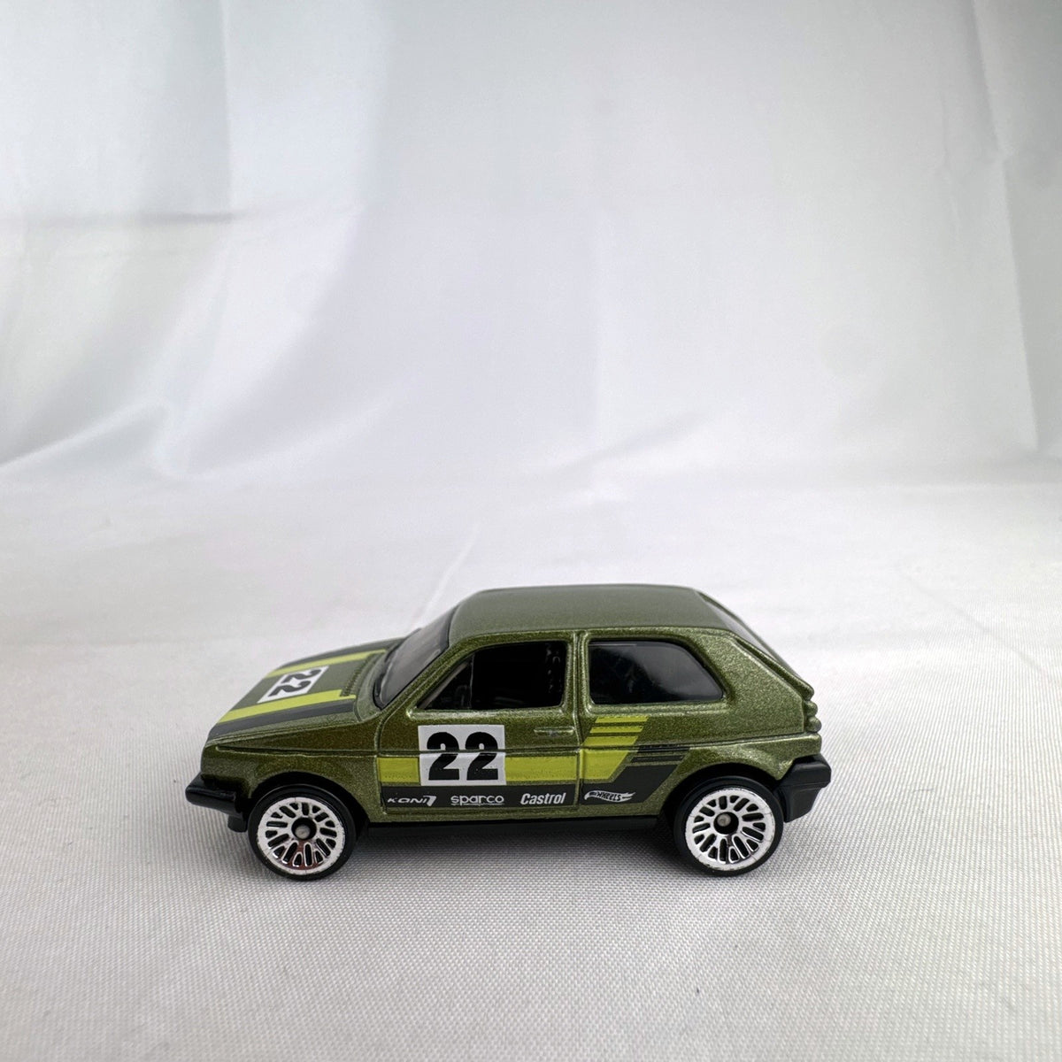 Hot Wheels 1:64 scale Volkswagen Golf Mk2 diecast car in metallic olive green with Castrol racing livery.