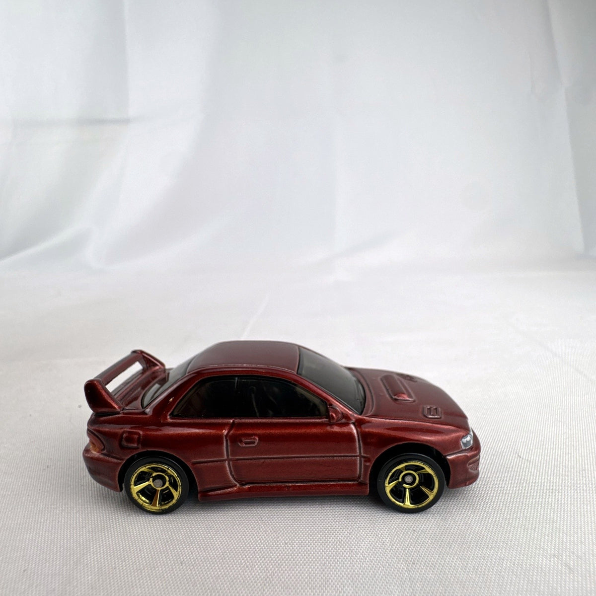 Hot Wheels 1:64 scale 1998 Subaru Impreza 22B STi-Version diecast car in dark metallic red with gold wheels