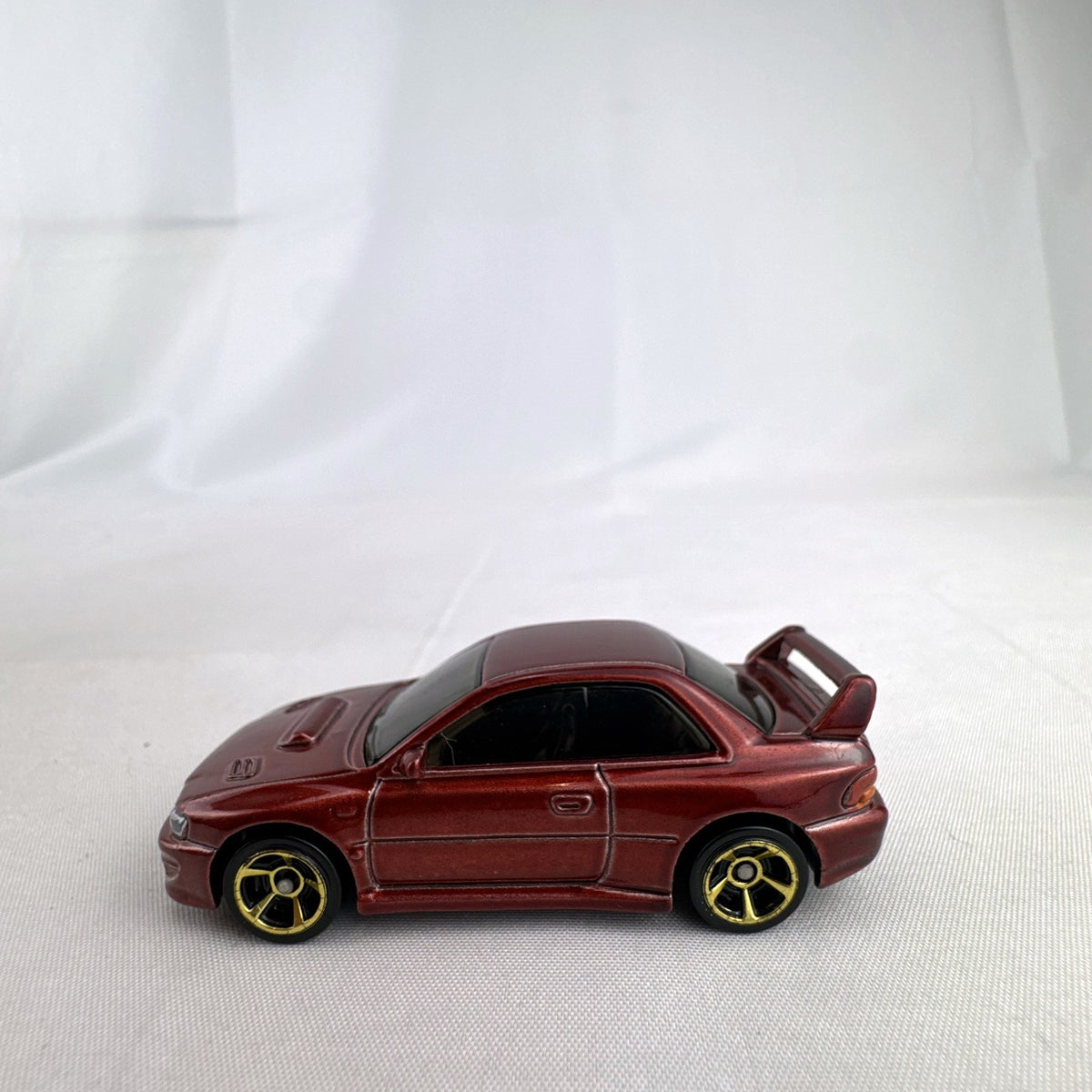 Hot Wheels 1:64 scale 1998 Subaru Impreza 22B STi-Version diecast car in dark metallic red with gold wheels