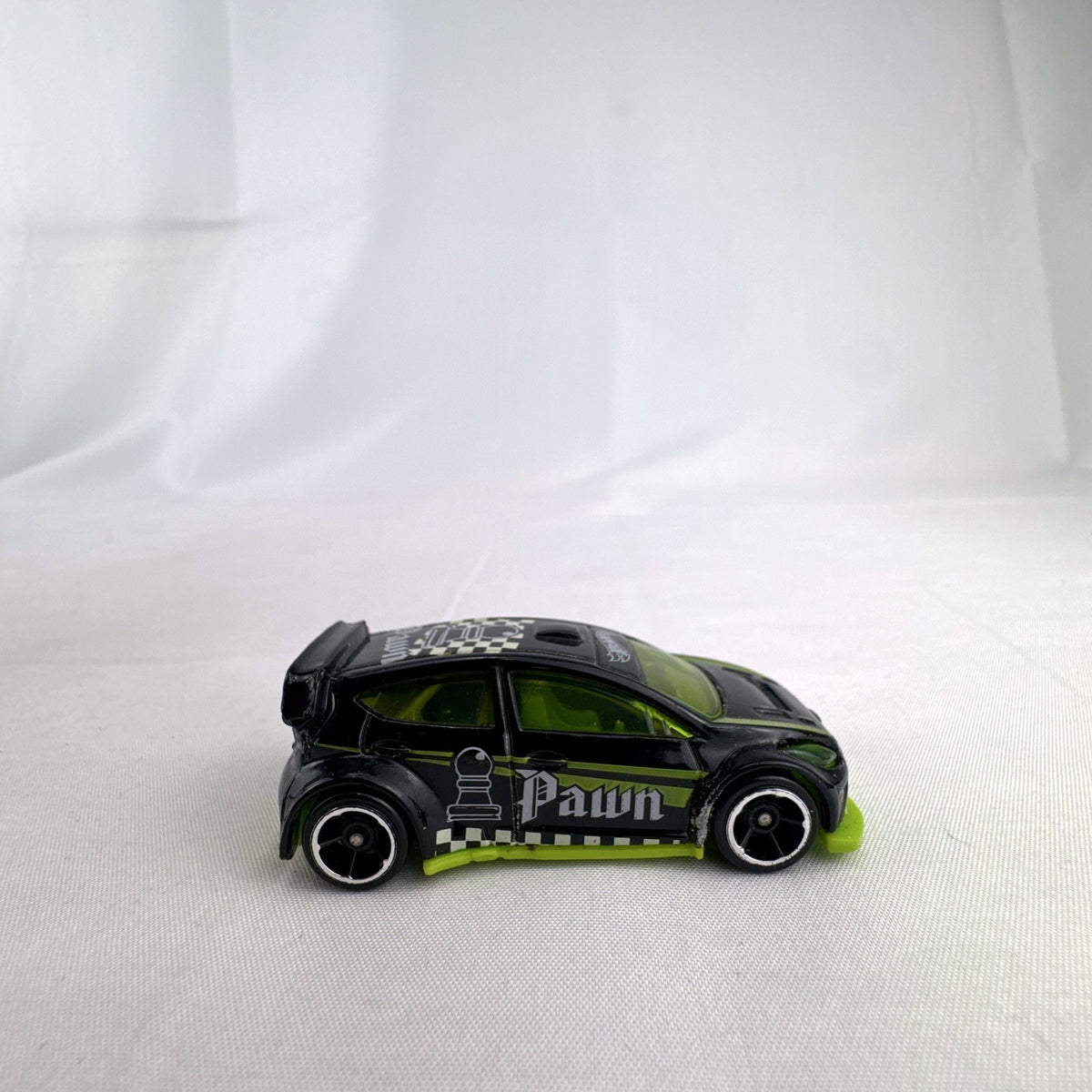 Hot Wheels 1:64 scale 2012 Ford Fiesta diecast car in black with green trim and HW Checkmate pawn graphics