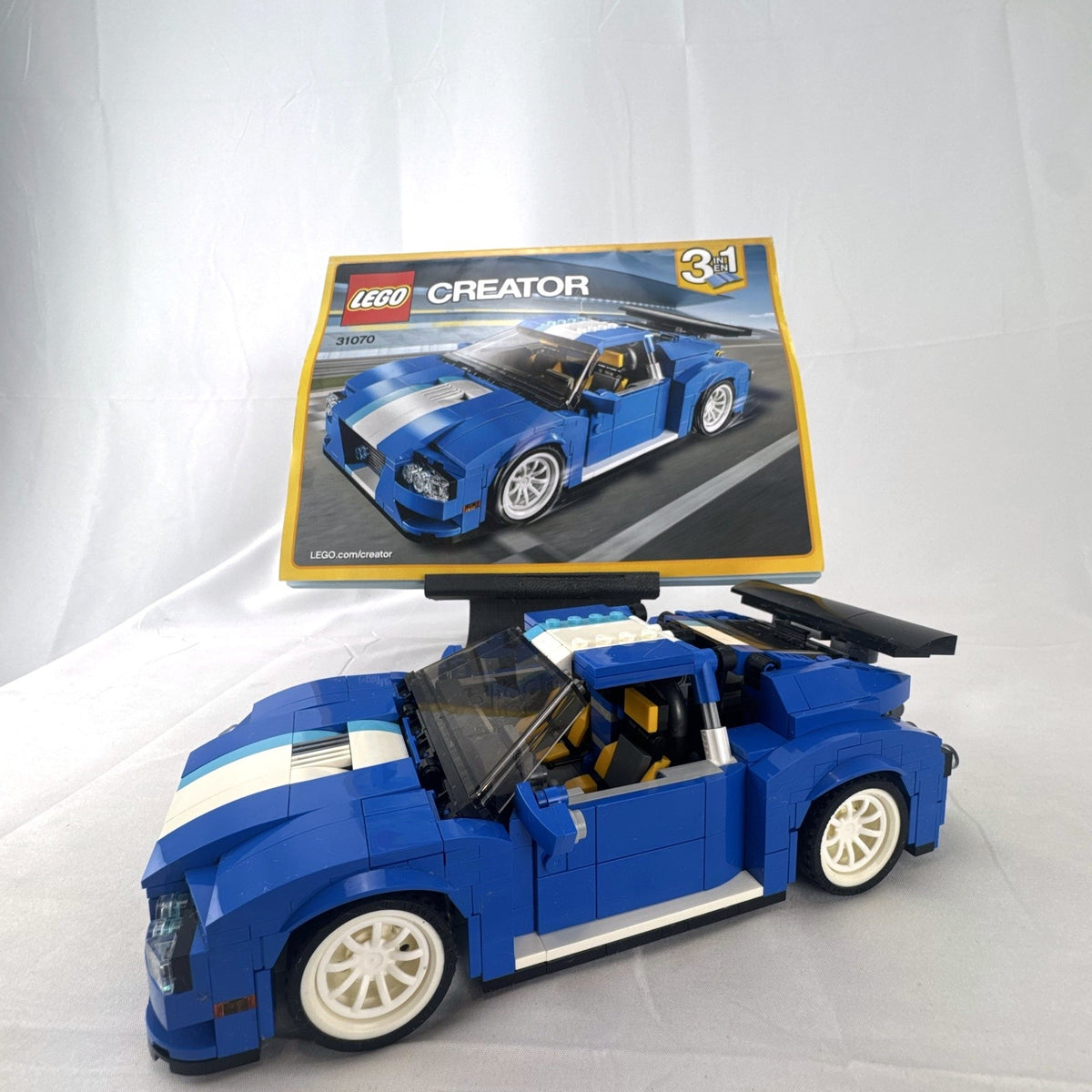 Assembled blue LEGO Creator 31070 Turbo Track Racer car with open gull-wing doors and instruction manual