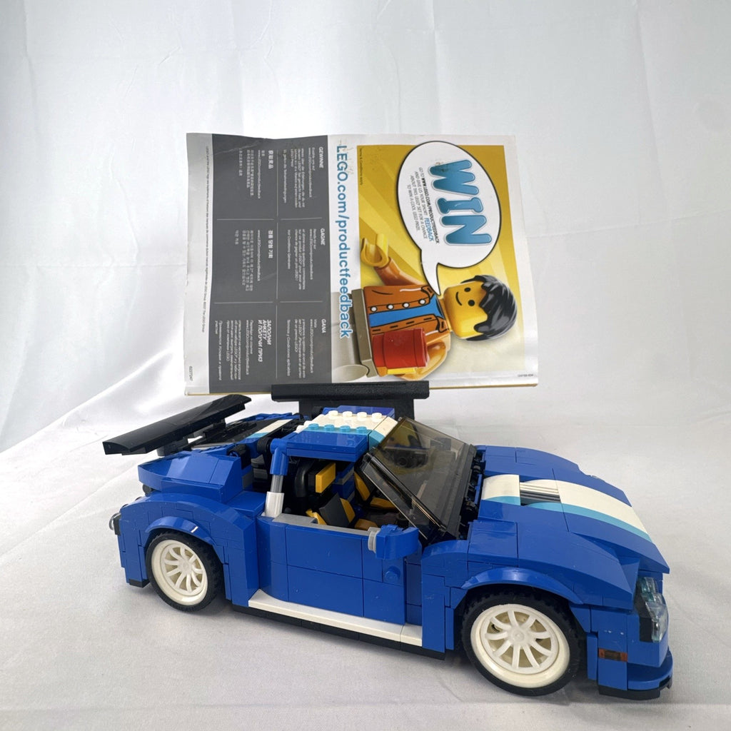 Assembled blue LEGO Creator 31070 Turbo Track Racer car with open gull-wing doors and instruction manual