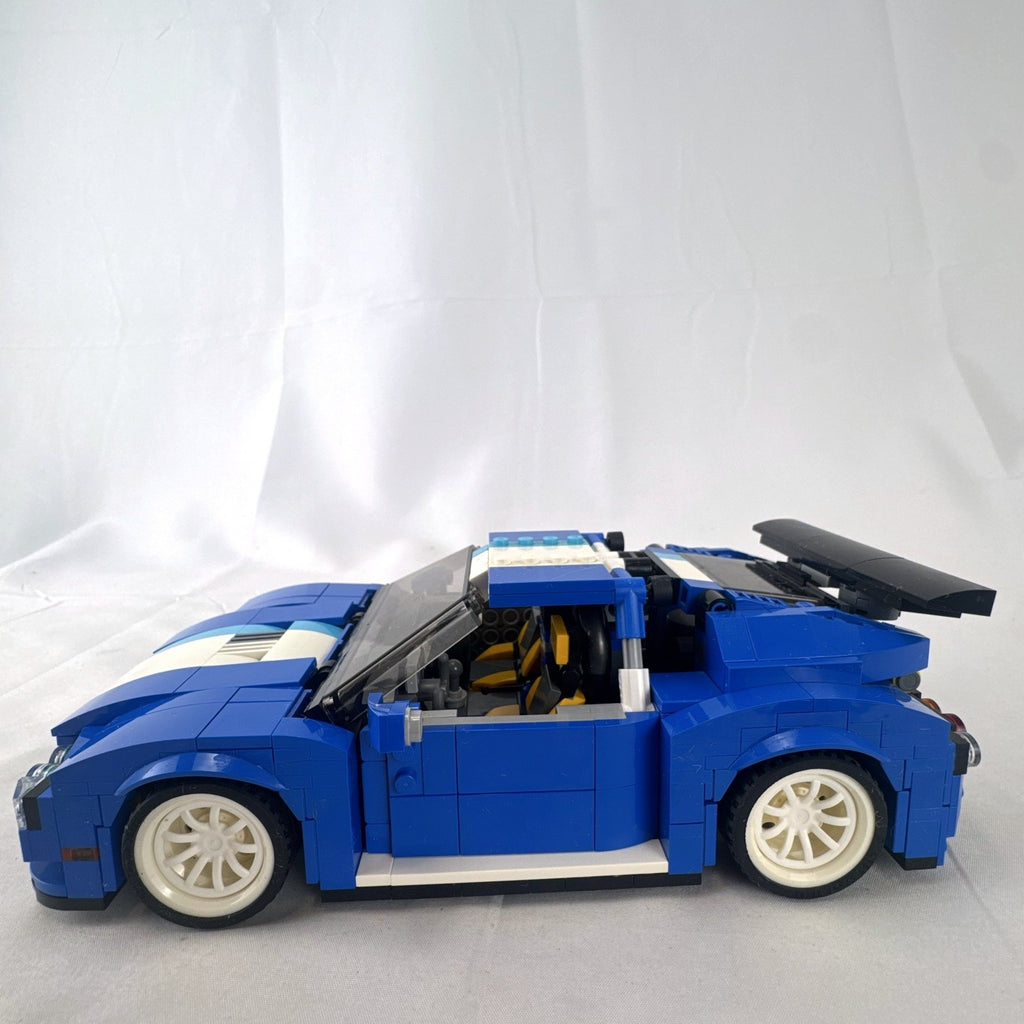 Assembled blue LEGO Creator 31070 Turbo Track Racer car with open gull-wing doors and instruction manual
