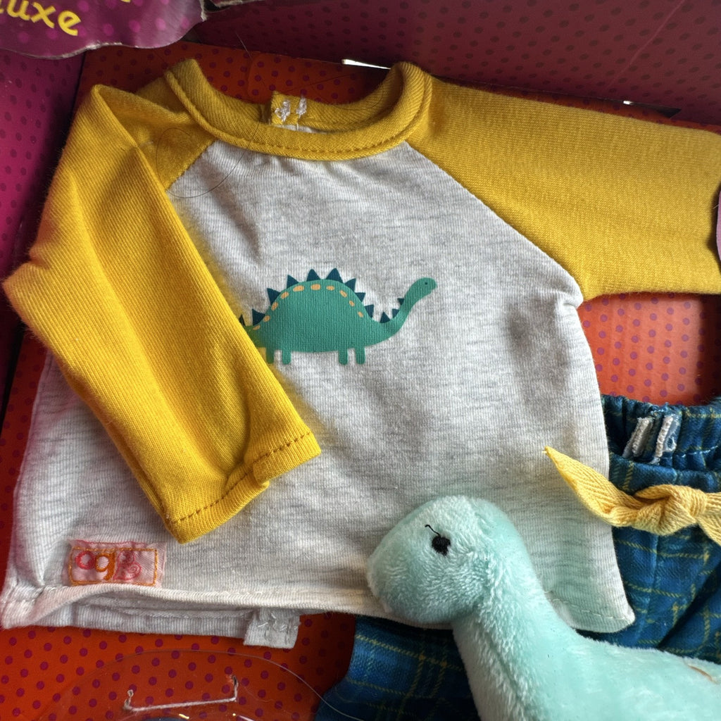 Our Generation Dino-Snores pajama outfit for 18-inch dolls in packaging with plaid pants and dinosaur plush.