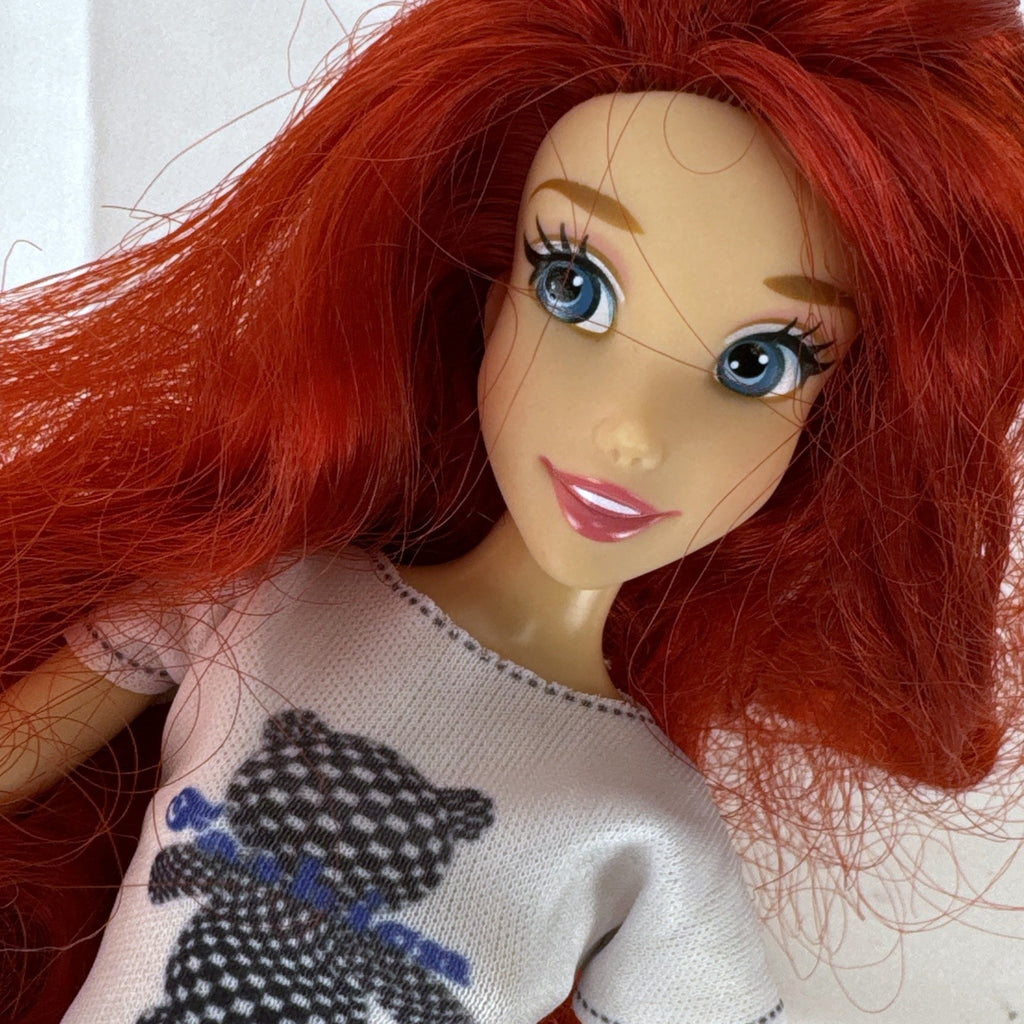 Articulated 11-inch Disney Ariel fashion doll with red hair in casual checkered pants and graphic t-shirt