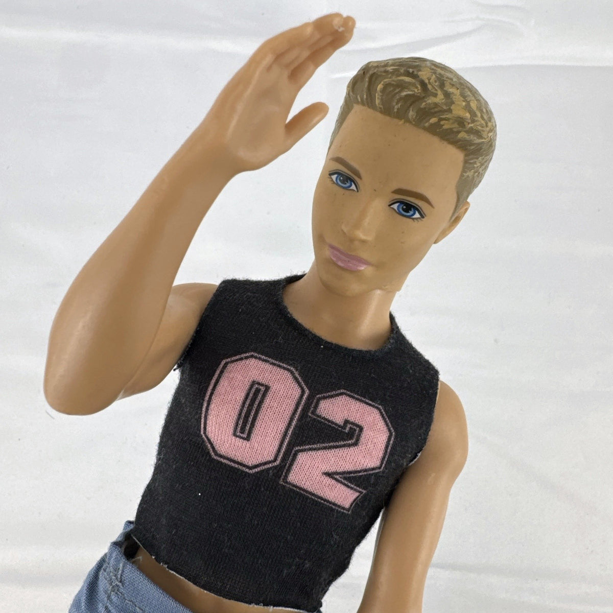 Mattel 12-inch Ken fashion doll with molded blonde hair, blue eyes, graphic sleeveless shirt, and blue trousers