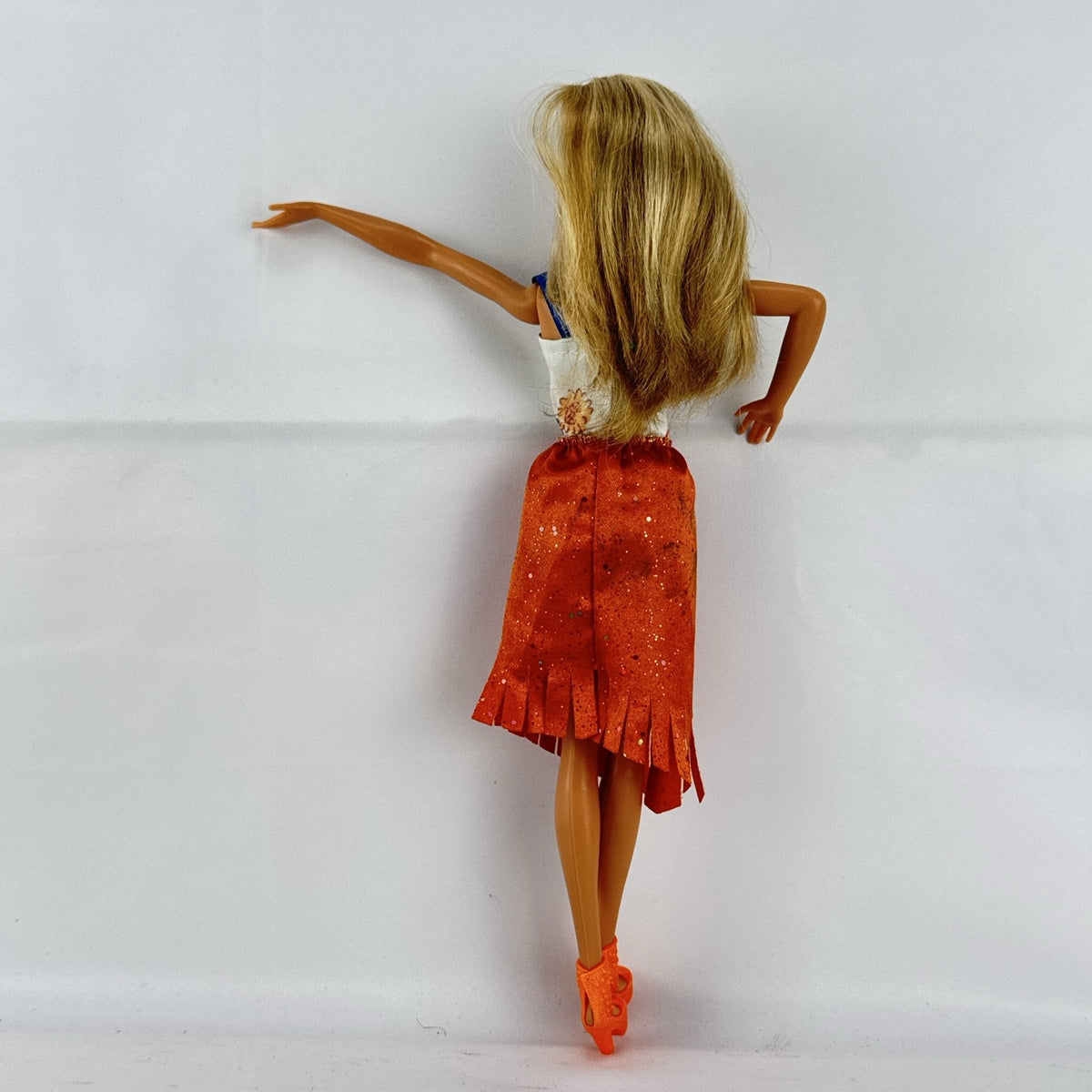 Mattel Barbie fashion doll with blonde hair wearing an orange fringe skirt and floral top