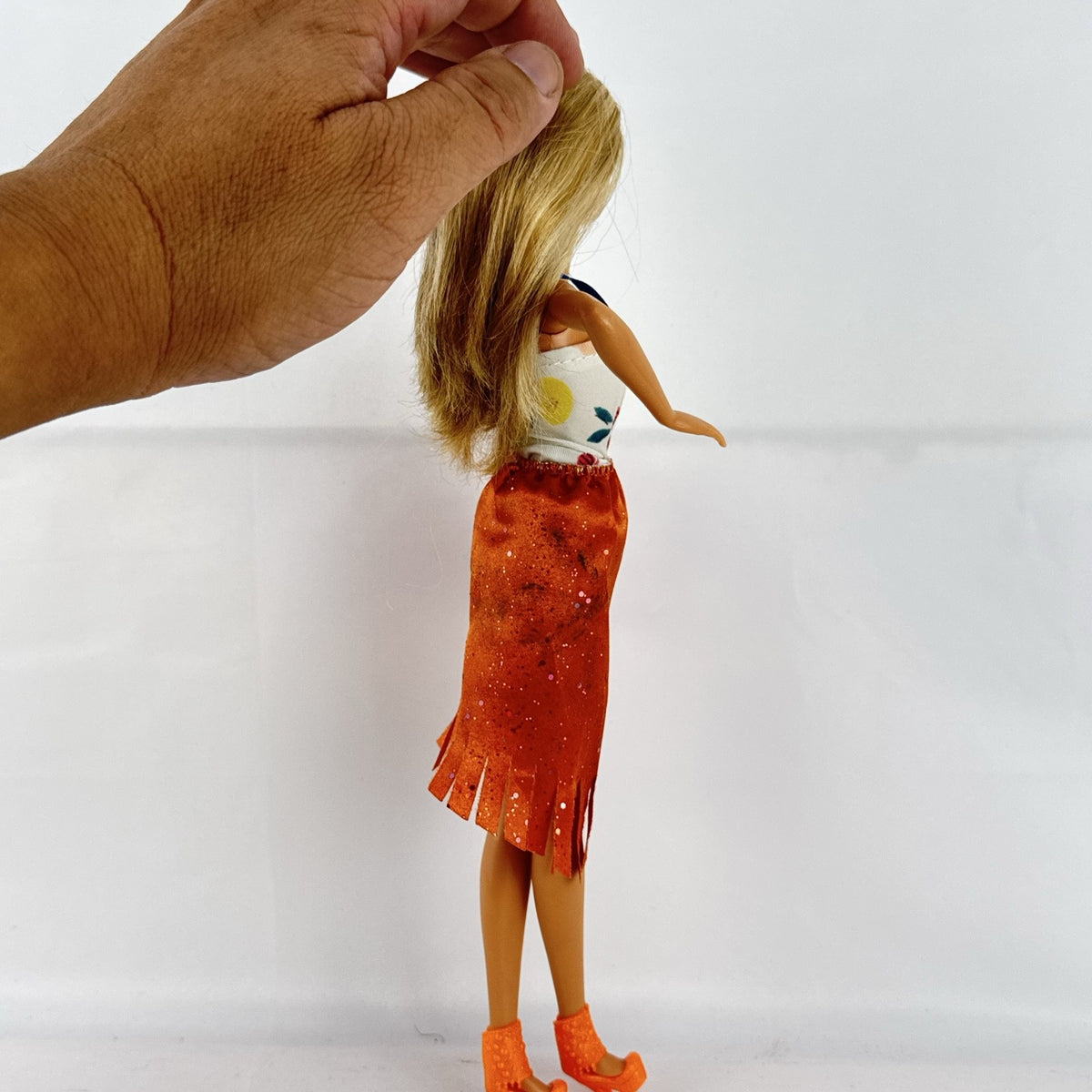Mattel Barbie fashion doll with blonde hair wearing an orange fringe skirt and floral top