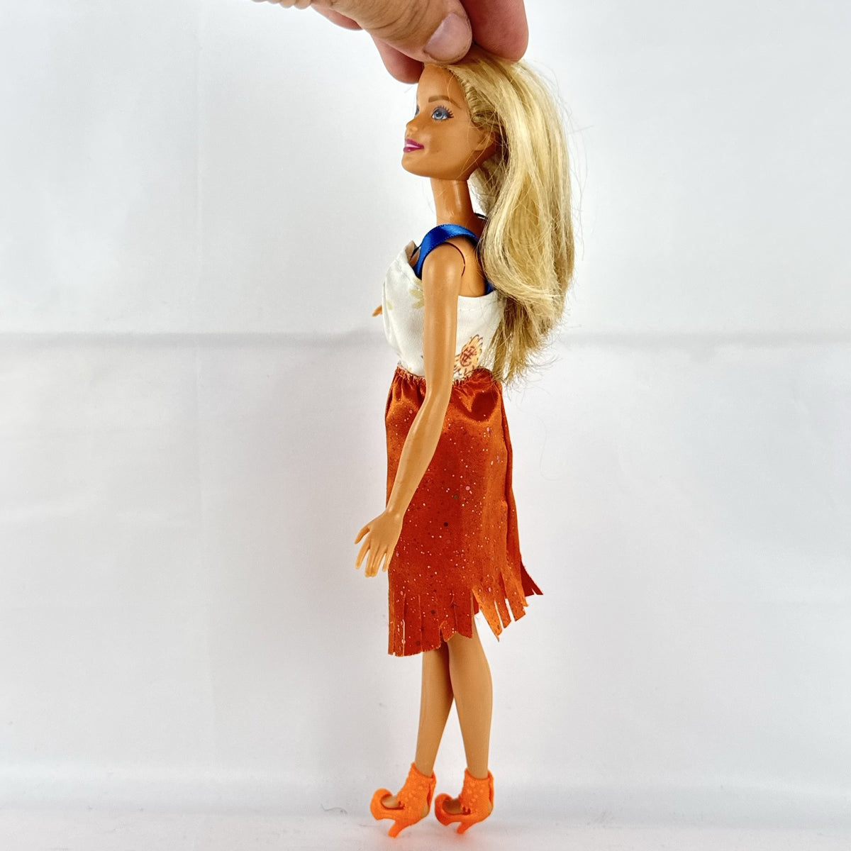 Mattel Barbie fashion doll with blonde hair wearing an orange fringe skirt and floral top