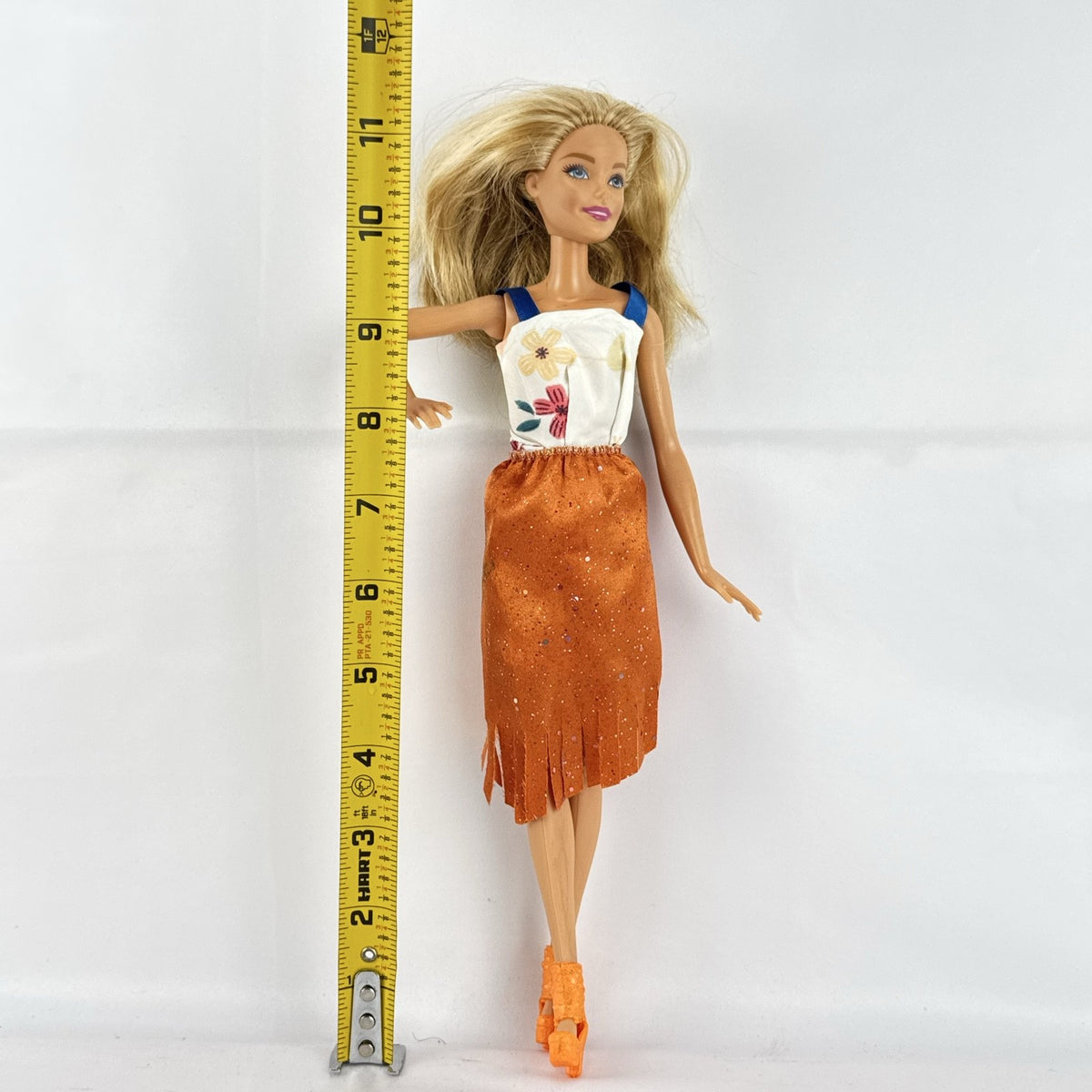Mattel Barbie fashion doll with blonde hair wearing an orange fringe skirt and floral top