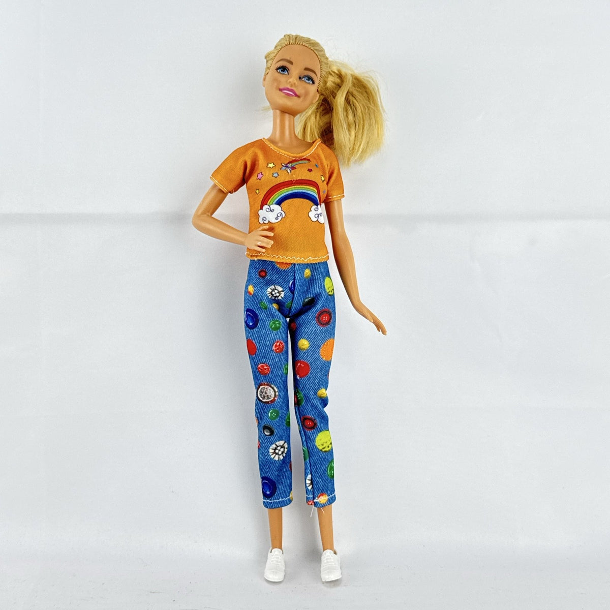 Mattel blonde Barbie doll wearing an orange rainbow shirt, button print pants, and white sneakers.