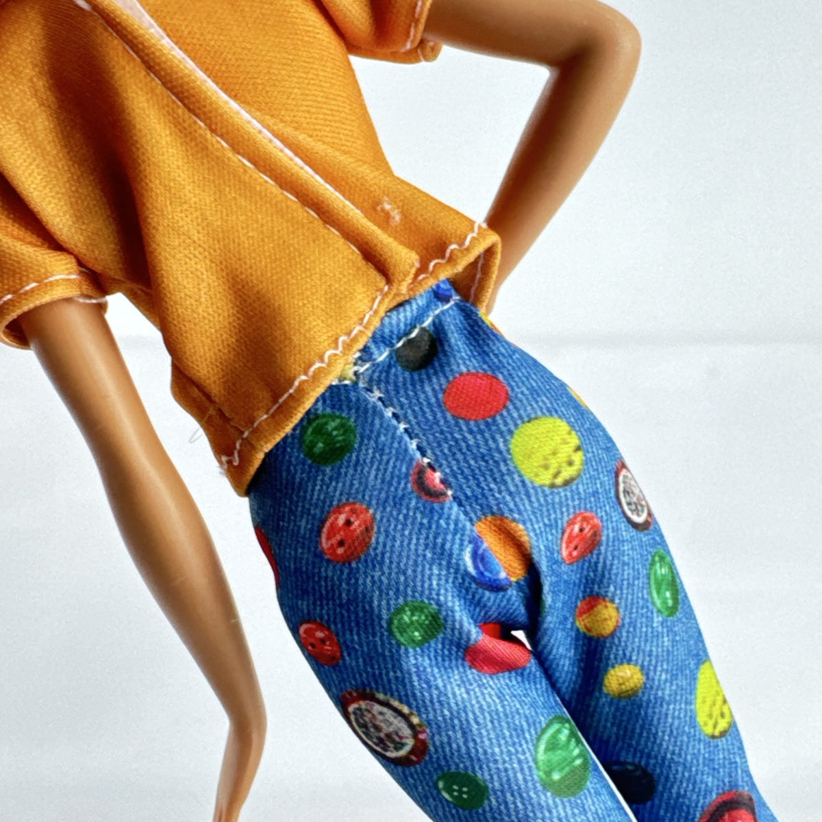 Mattel blonde Barbie doll wearing an orange rainbow shirt, button print pants, and white sneakers.