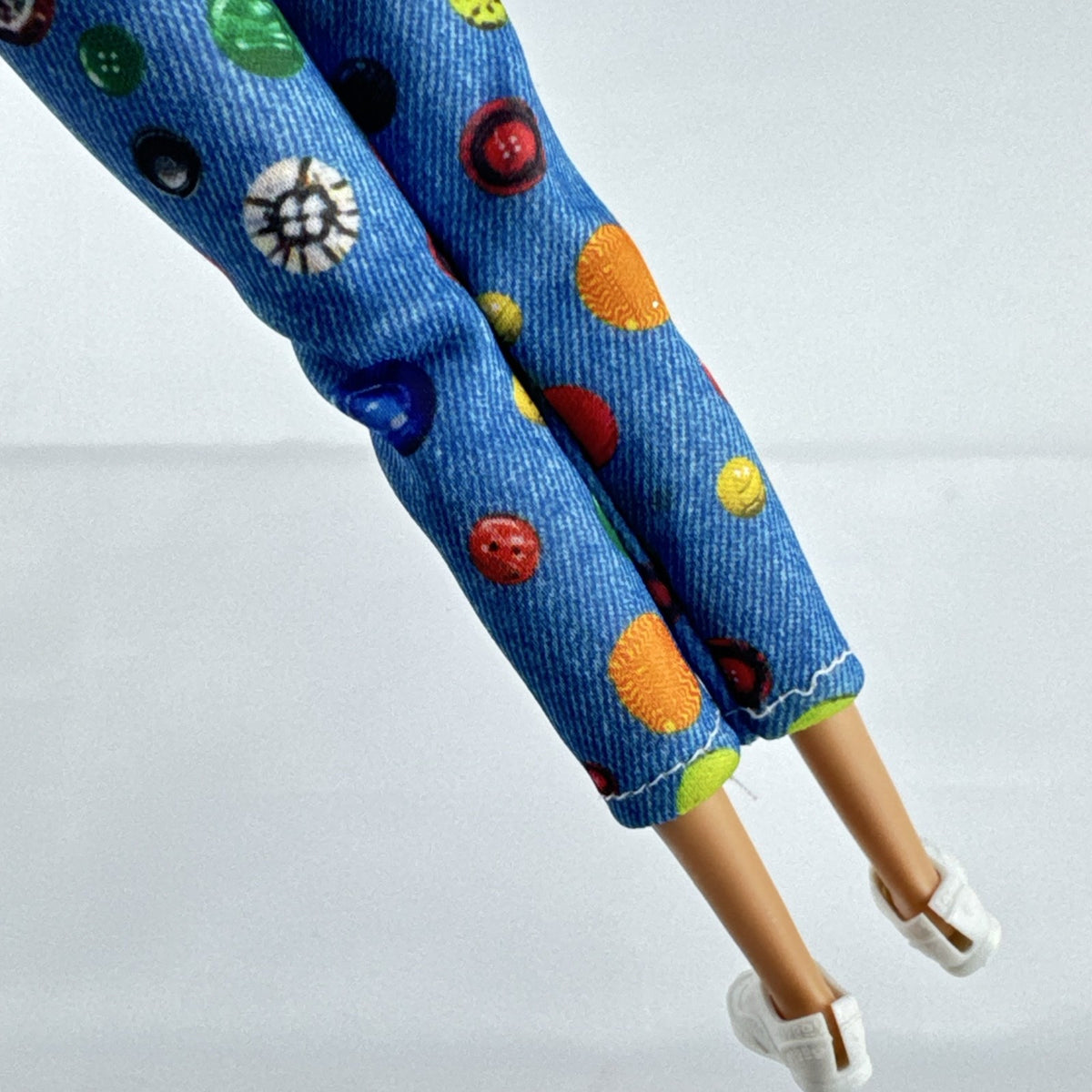 Mattel blonde Barbie doll wearing an orange rainbow shirt, button print pants, and white sneakers.