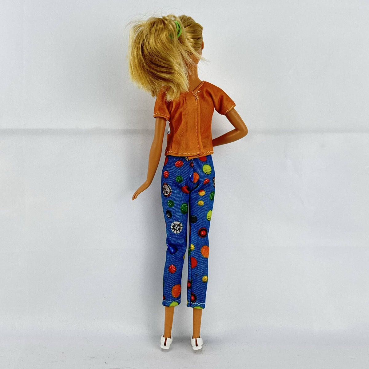Mattel blonde Barbie doll wearing an orange rainbow shirt, button print pants, and white sneakers.