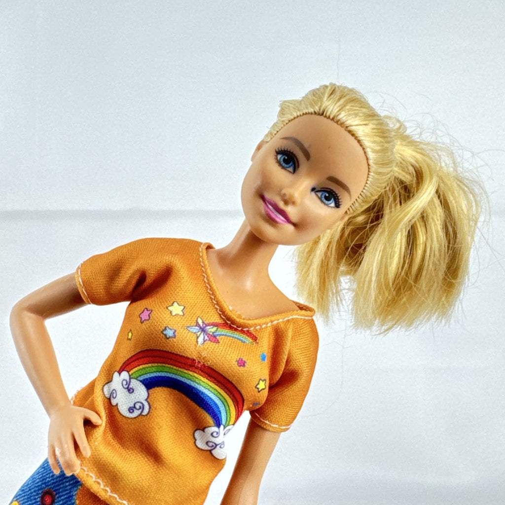 Mattel blonde Barbie doll wearing an orange rainbow shirt, button print pants, and white sneakers.
