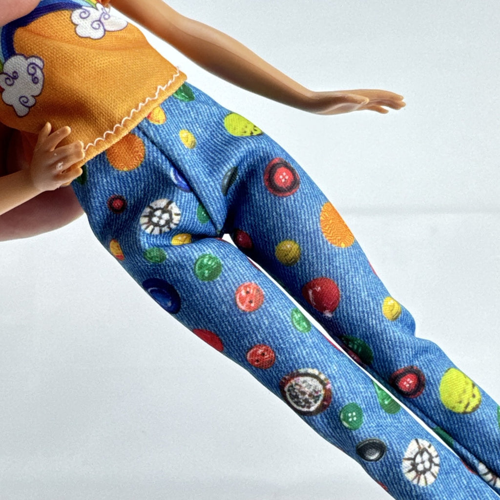 Mattel blonde Barbie doll wearing an orange rainbow shirt, button print pants, and white sneakers.