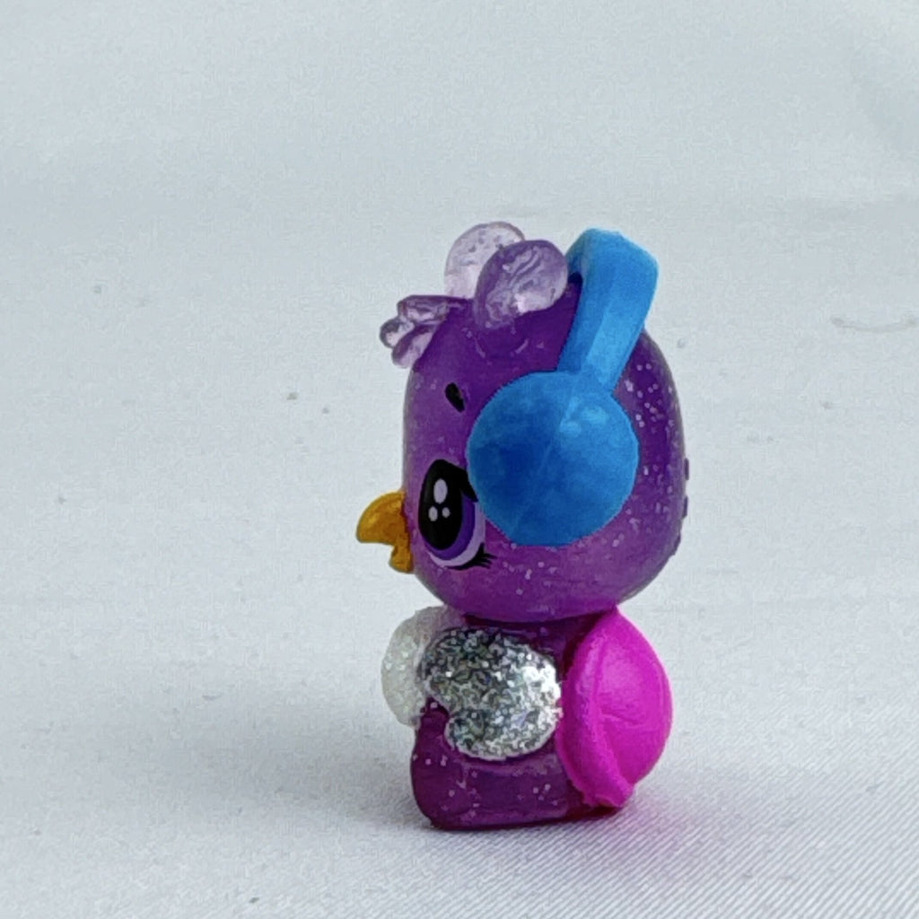 Spin Master Hatchimals CollEGGtibles miniature purple glitter penguin figure wearing molded blue earmuffs.