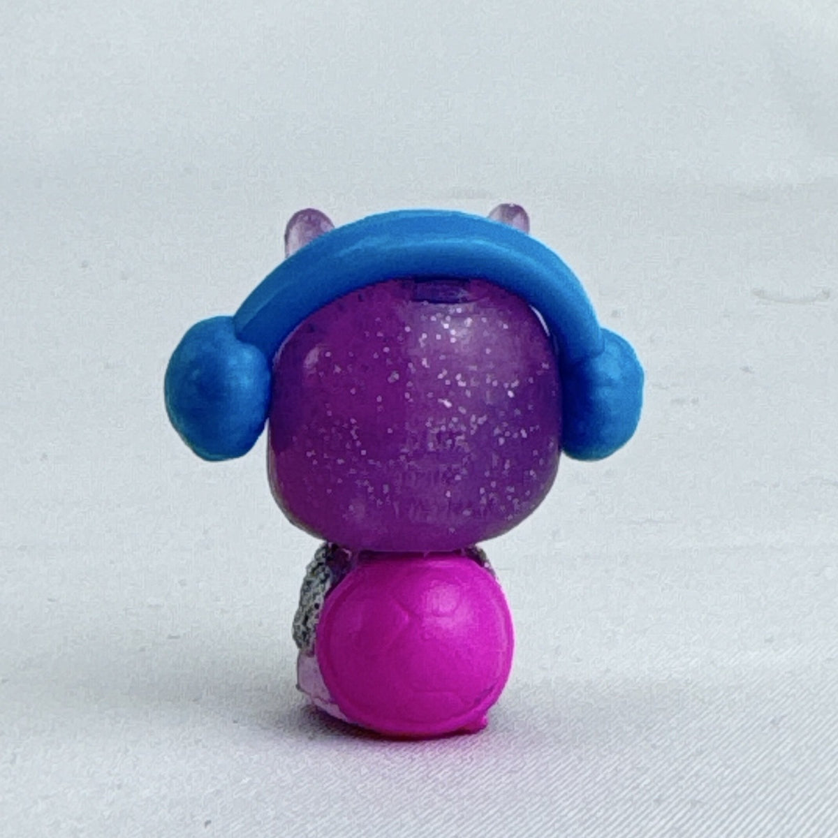 Spin Master Hatchimals CollEGGtibles miniature purple glitter penguin figure wearing molded blue earmuffs.