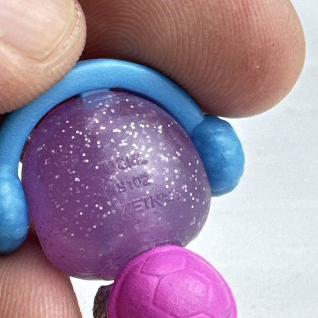 Spin Master Hatchimals CollEGGtibles miniature purple glitter penguin figure wearing molded blue earmuffs.