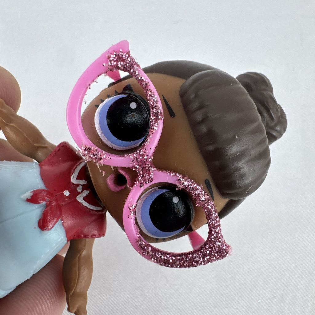 MGA L.O.L. Surprise! 3-inch doll with brown hair bun, pink glitter cat-eye glasses, and red tie-front outfit