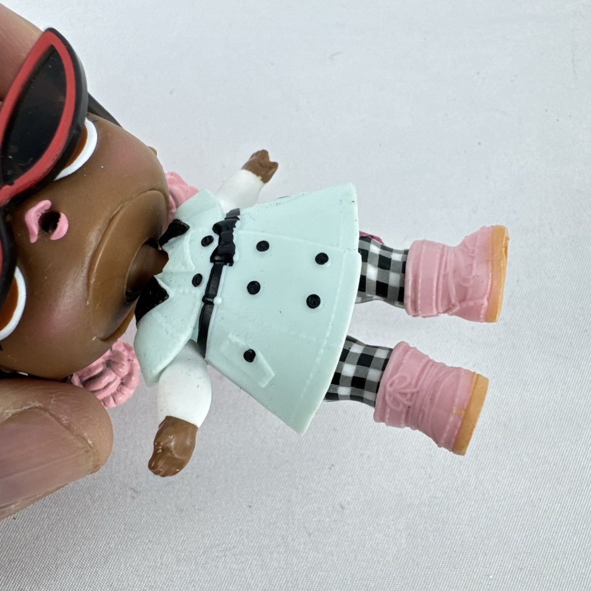 MGA L.O.L. Surprise Jet Set Q.T. 3-inch doll wearing a mint green trench coat, red sunglasses, and pink boots