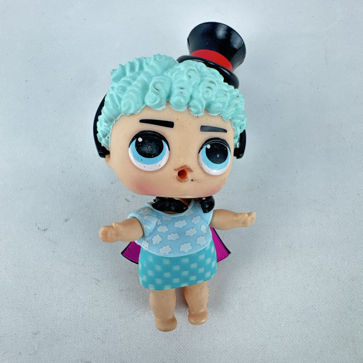 MGA Entertainment L.O.L. Surprise! The Great Baby doll with curly turquoise hair, top hat headband, and black cape.