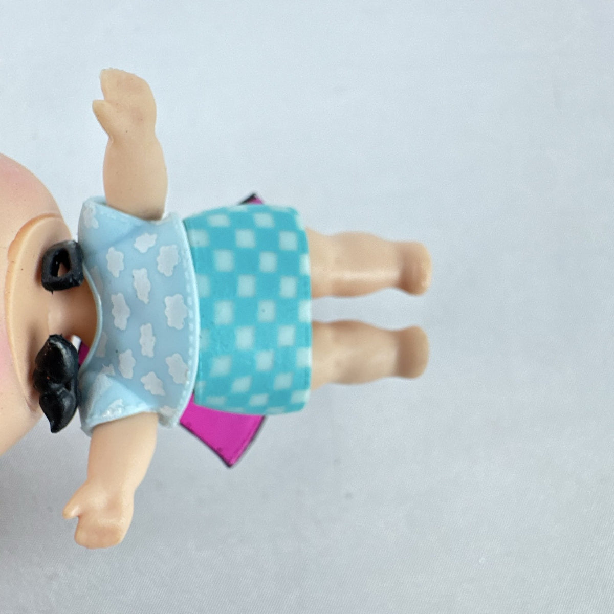 MGA Entertainment L.O.L. Surprise! The Great Baby doll with curly turquoise hair, top hat headband, and black cape.