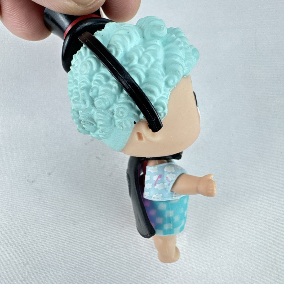 MGA Entertainment L.O.L. Surprise! The Great Baby doll with curly turquoise hair, top hat headband, and black cape.
