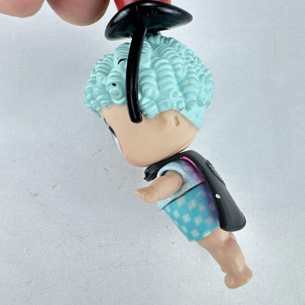 MGA Entertainment L.O.L. Surprise! The Great Baby doll with curly turquoise hair, top hat headband, and black cape.