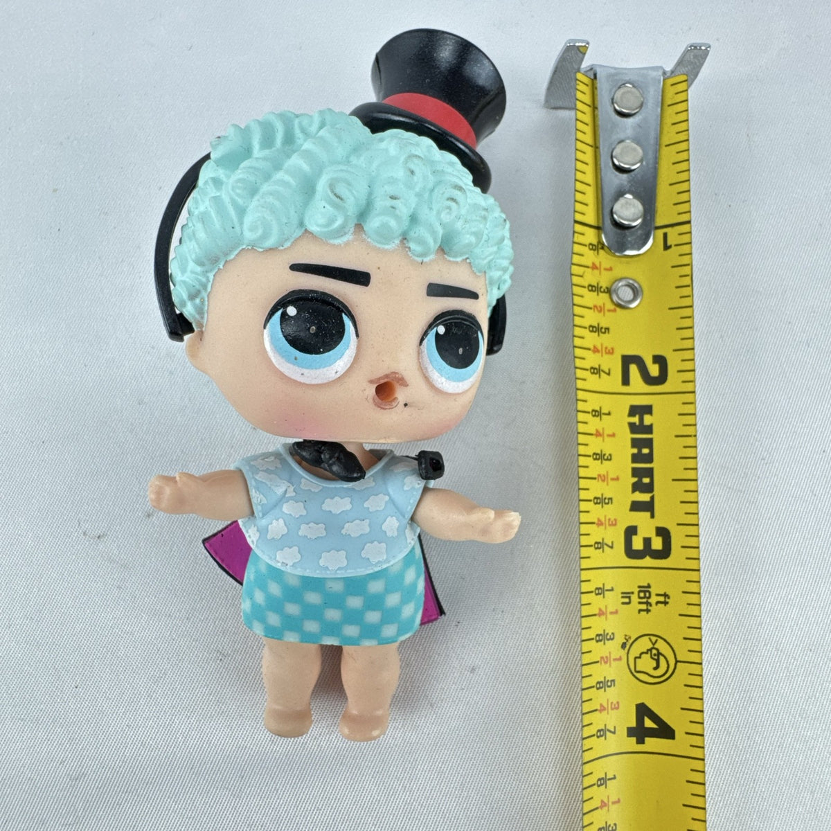 MGA Entertainment L.O.L. Surprise! The Great Baby doll with curly turquoise hair, top hat headband, and black cape.