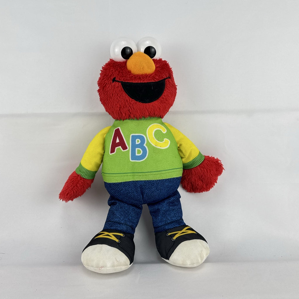 Hasbro Sesame Street ABC Elmo 12-inch plush toy wearing a colorblock alphabet shirt and sneakers.