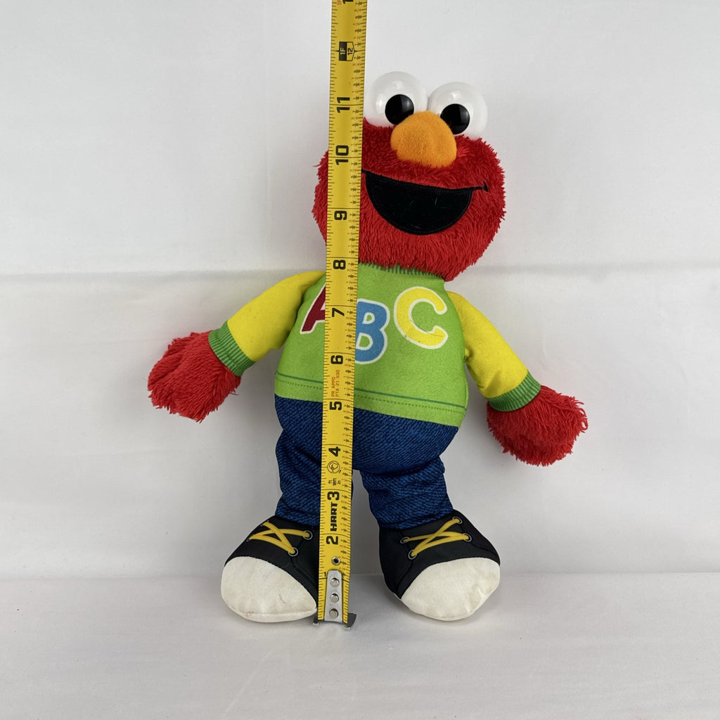 Hasbro Sesame Street ABC Elmo 12-inch plush toy wearing a colorblock alphabet shirt and sneakers.