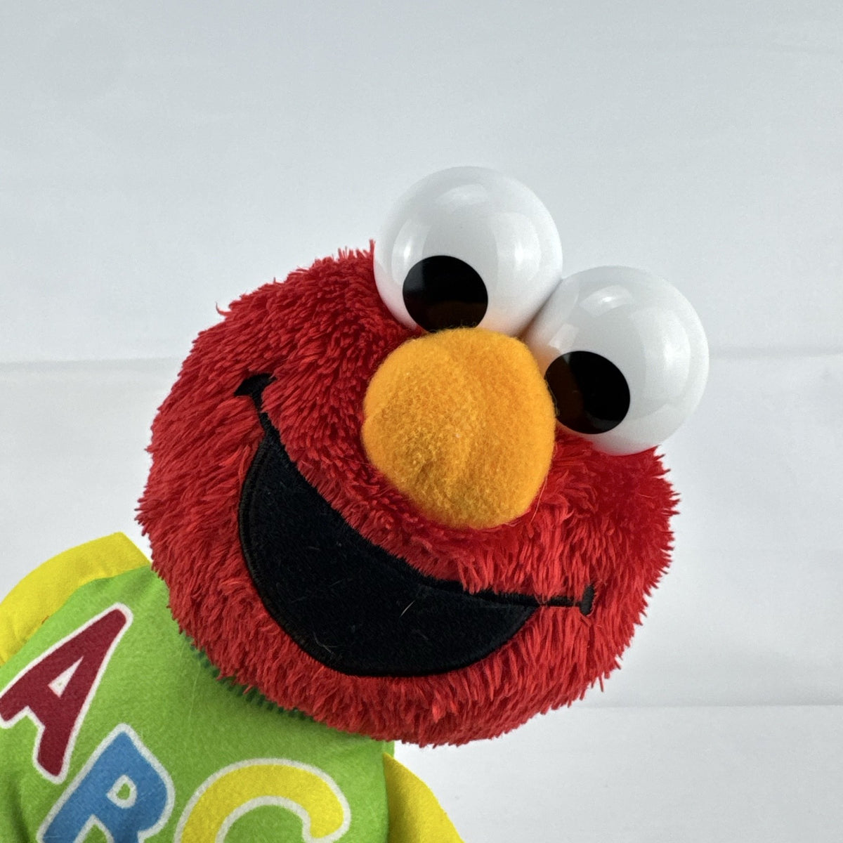 Hasbro Sesame Street ABC Elmo 12-inch plush toy wearing a colorblock alphabet shirt and sneakers.