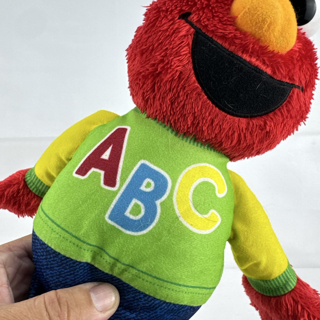 Hasbro Sesame Street ABC Elmo 12-inch plush toy wearing a colorblock alphabet shirt and sneakers.