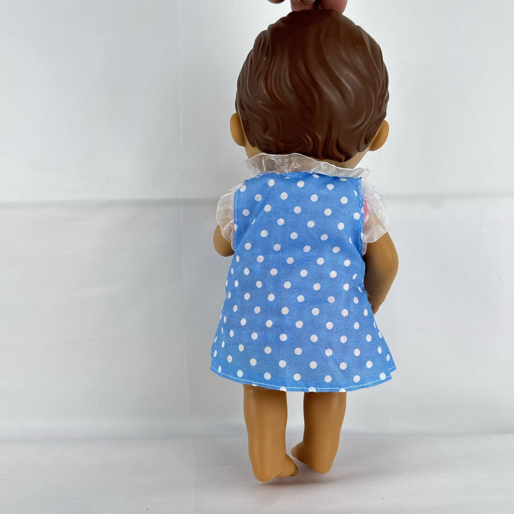Hasbro Baby Alive 11-inch vinyl baby doll with molded brown hair, brown eyes, and blue polka dot dress