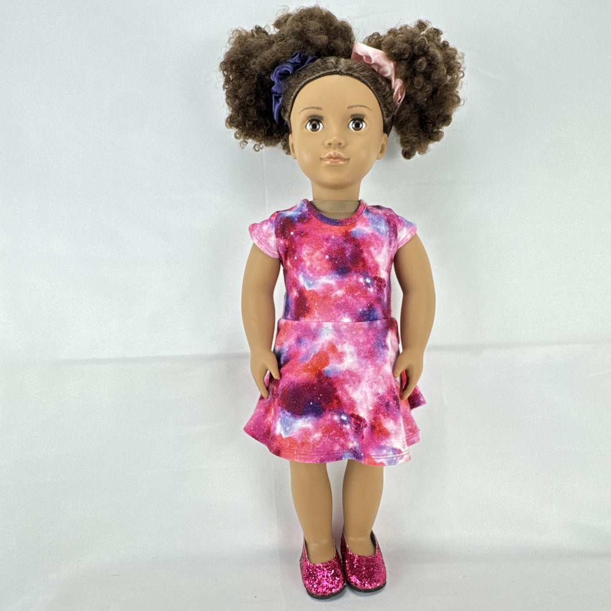 Our Generation 18-inch doll with brown afro puffs wearing a pink galaxy print dress and glitter shoes
