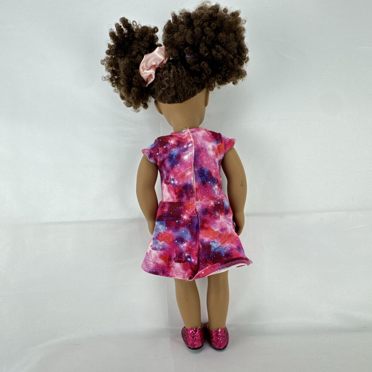 Our Generation 18-inch doll with brown afro puffs wearing a pink galaxy print dress and glitter shoes