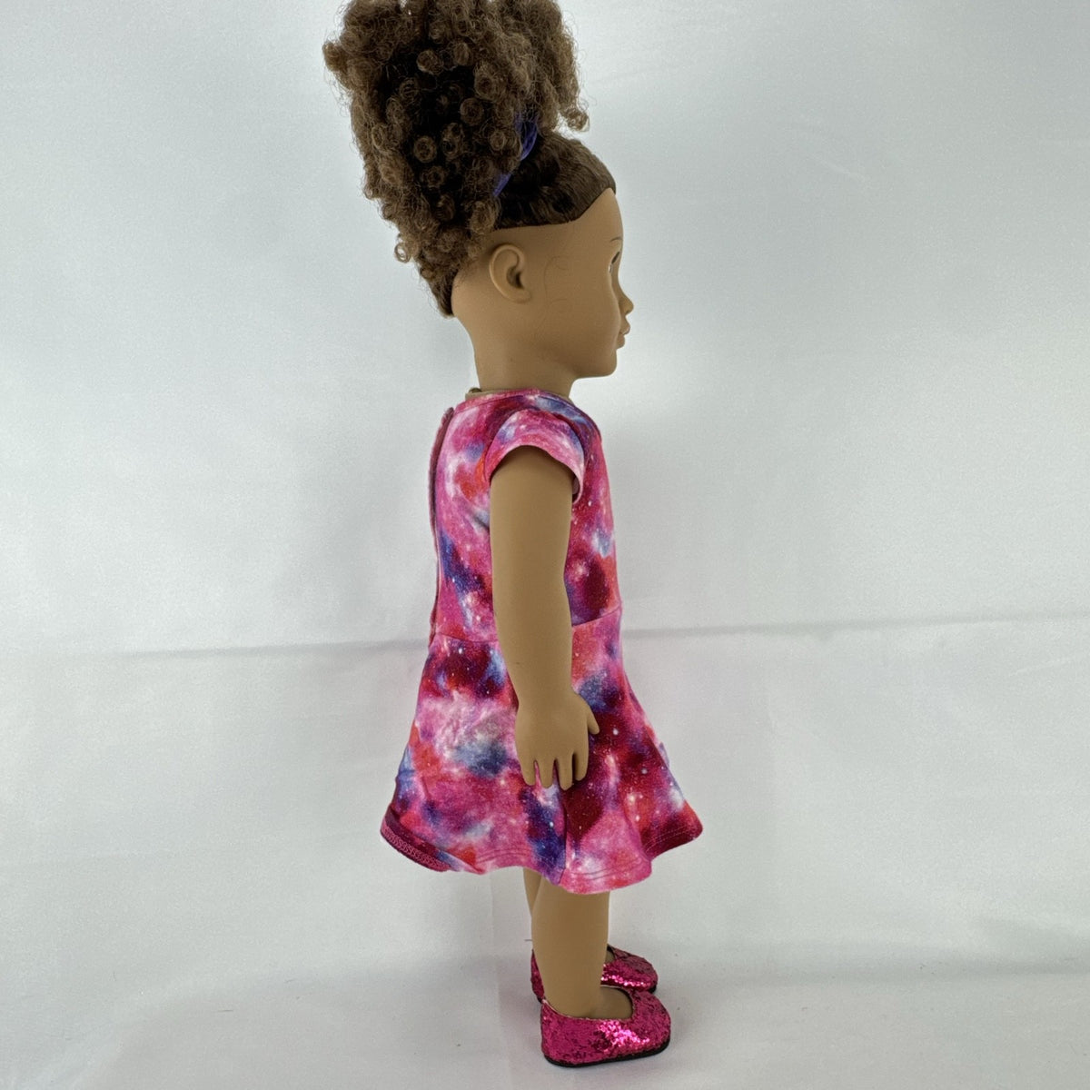 Our Generation 18-inch doll with brown afro puffs wearing a pink galaxy print dress and glitter shoes