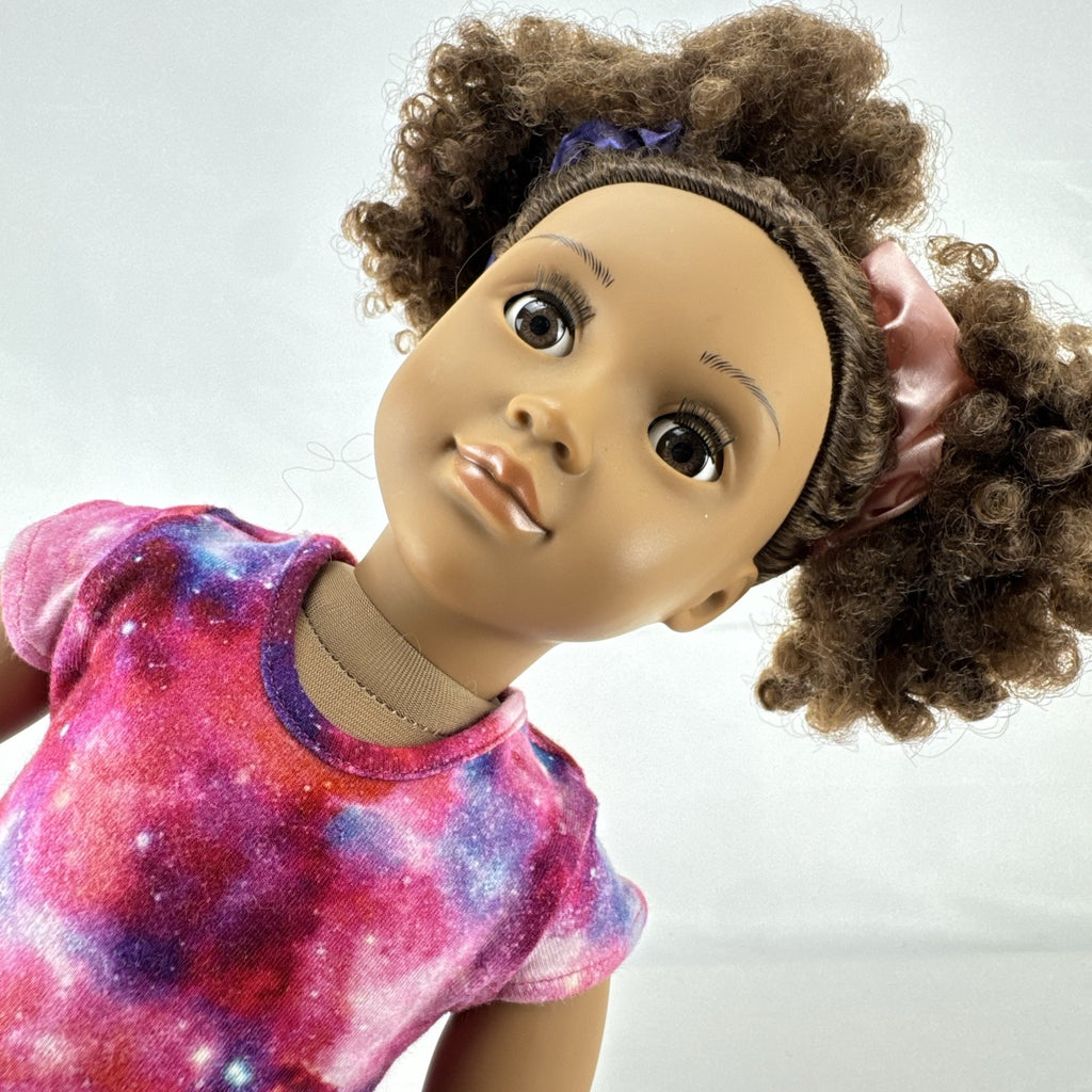Our Generation 18-inch doll with brown afro puffs wearing a pink galaxy print dress and glitter shoes