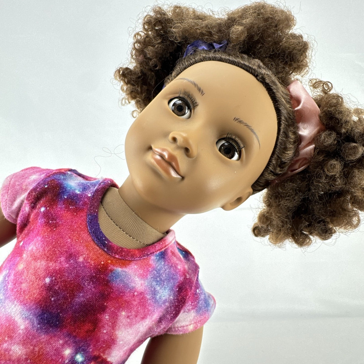 Our Generation 18-inch doll with brown afro puffs wearing a pink galaxy print dress and glitter shoes