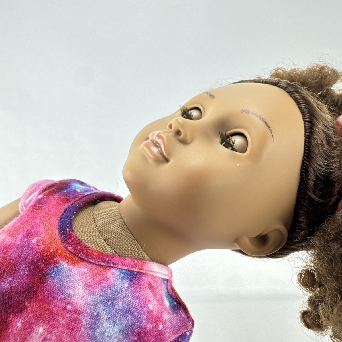 Our Generation 18-inch doll with brown afro puffs wearing a pink galaxy print dress and glitter shoes