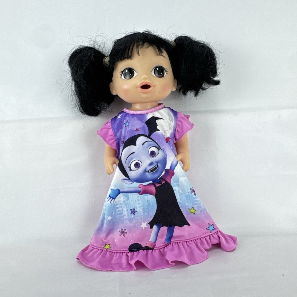 Hasbro Baby Alive 12-inch doll with black pigtails wearing a colorful Disney Vampirina dress