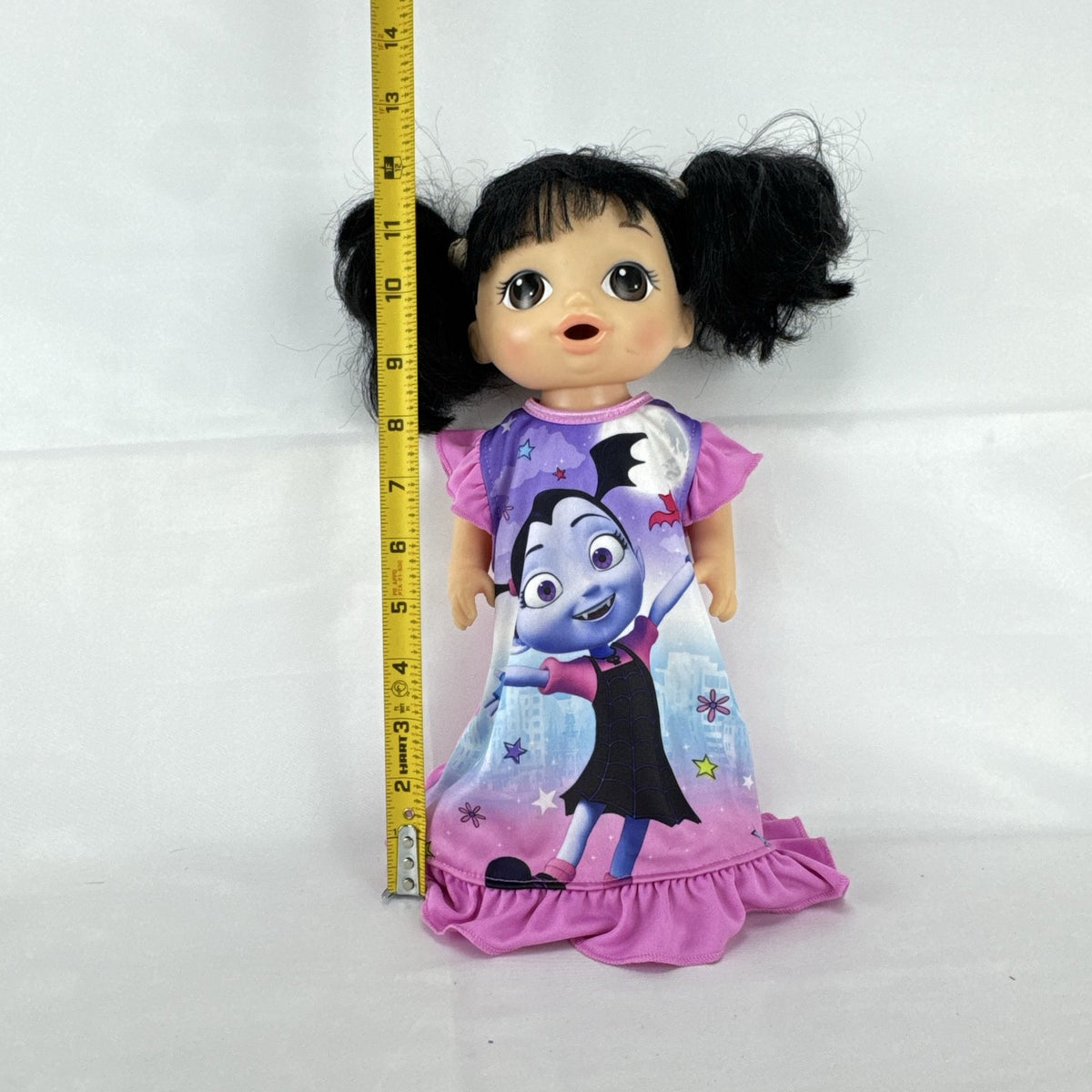 Hasbro Baby Alive 12-inch doll with black pigtails wearing a colorful Disney Vampirina dress