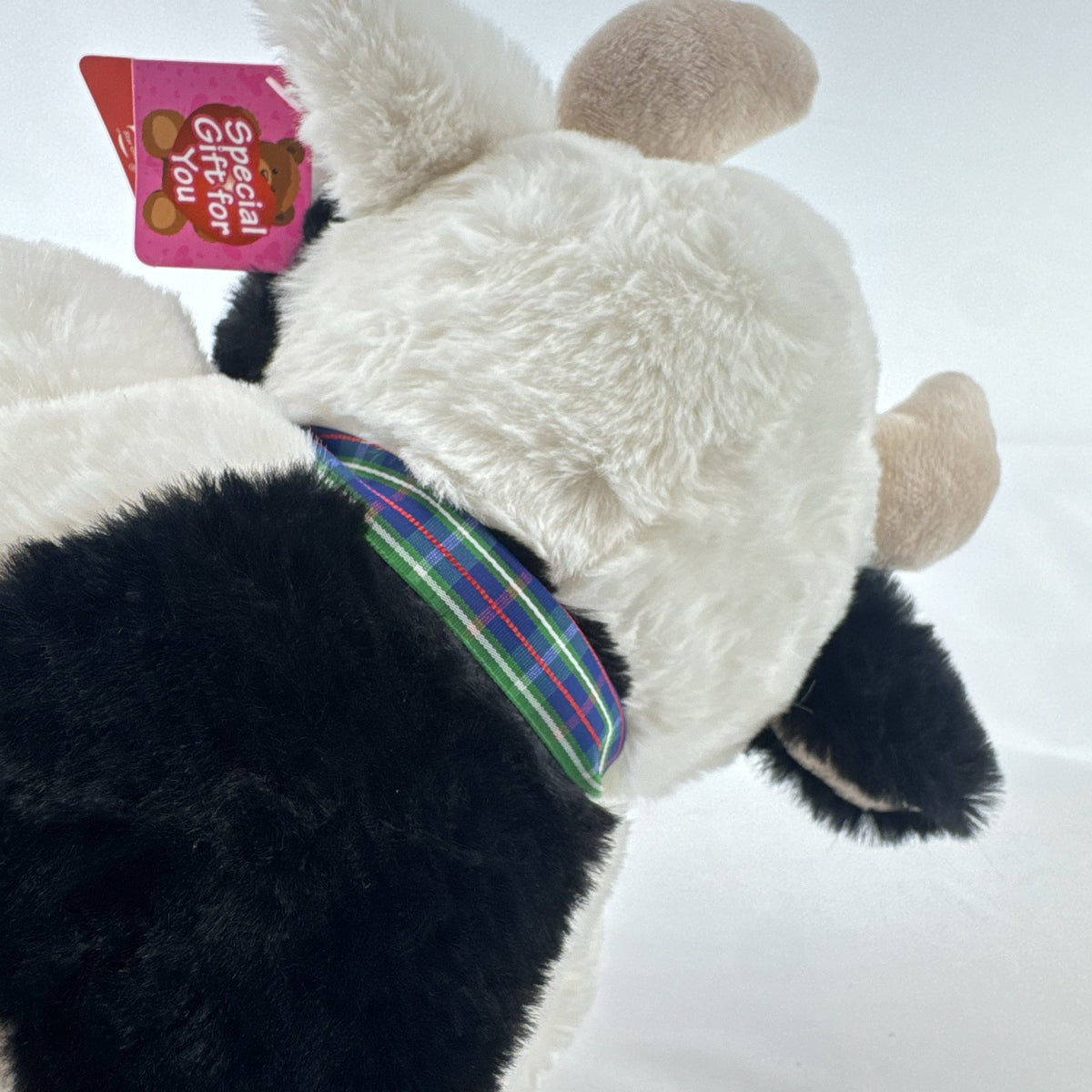 Star Gifts 13-inch black and white Holstein cow plush wearing a green plaid ribbon and jingle bell