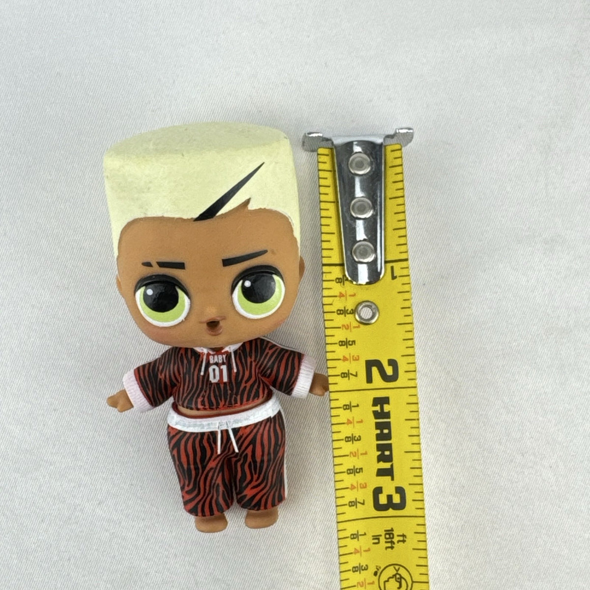 MGA L.O.L. Surprise Boys Swaggy 3-inch mini doll with blonde flocked hair and red tracksuit.