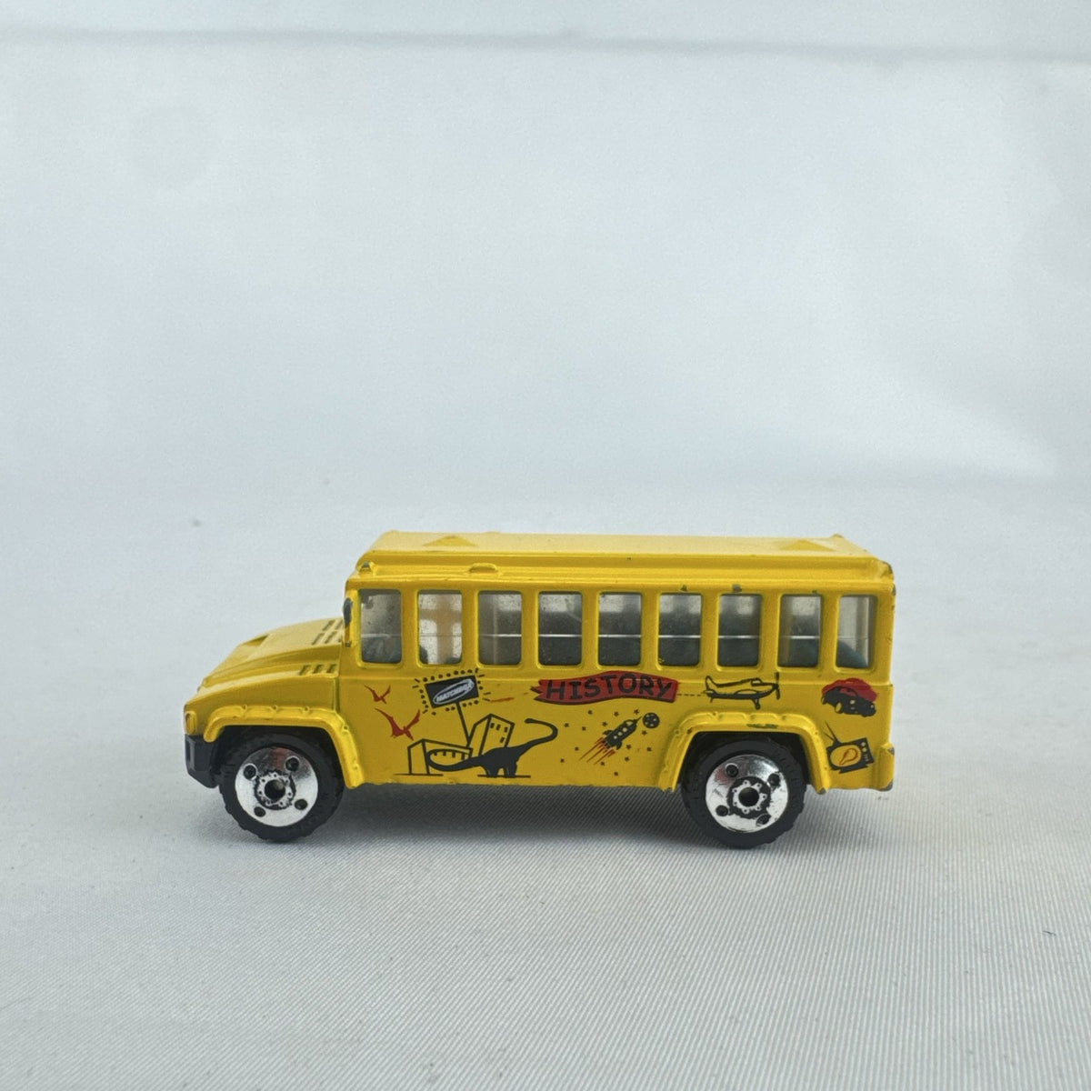 Matchbox 1:64 scale yellow diecast school bus with History dinosaur and rocket graphics